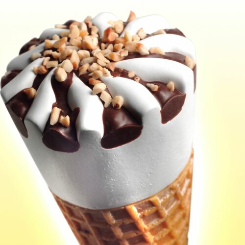 Cono gelato a cialda con crema bianca decorata con cioccolato e granella di nocciole; sfondo giallo chiaro.