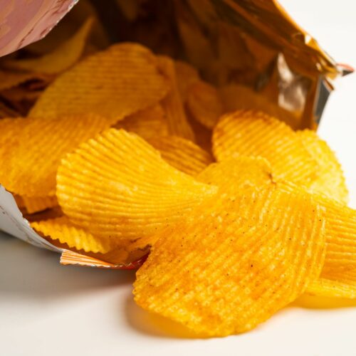 Patatine fritte rigate dorate che fuoriescono da un sacchetto aperto.