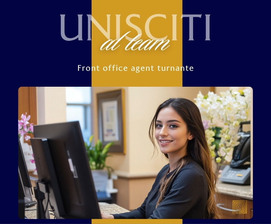 Una giovane donna al banco della reception in un ufficio, seduta davanti al computer e sorridente, con decorazioni e piante sullo sfondo.